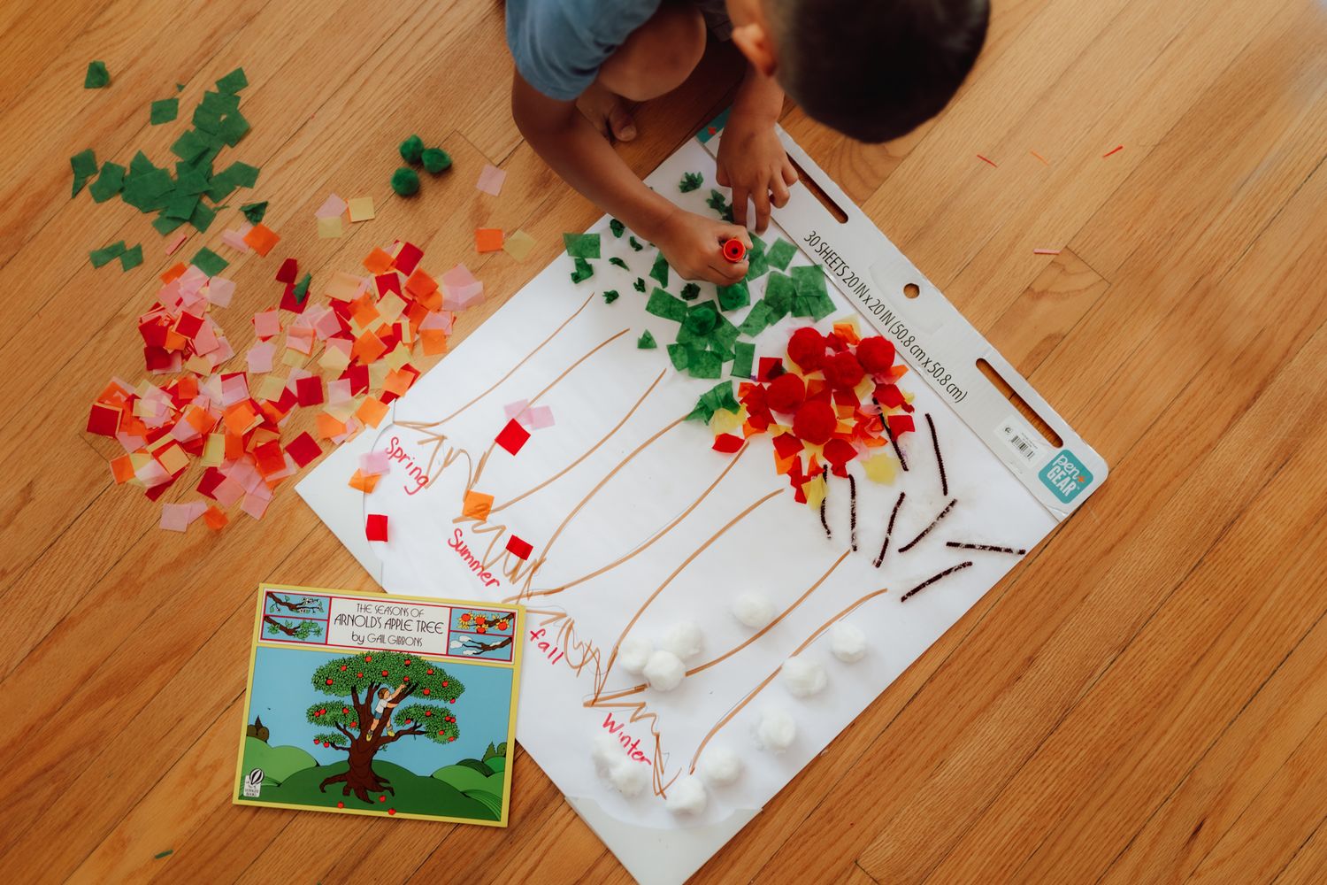 Art supplies and paper decorations scattered on wooden floor beneath wall-mounted world map.