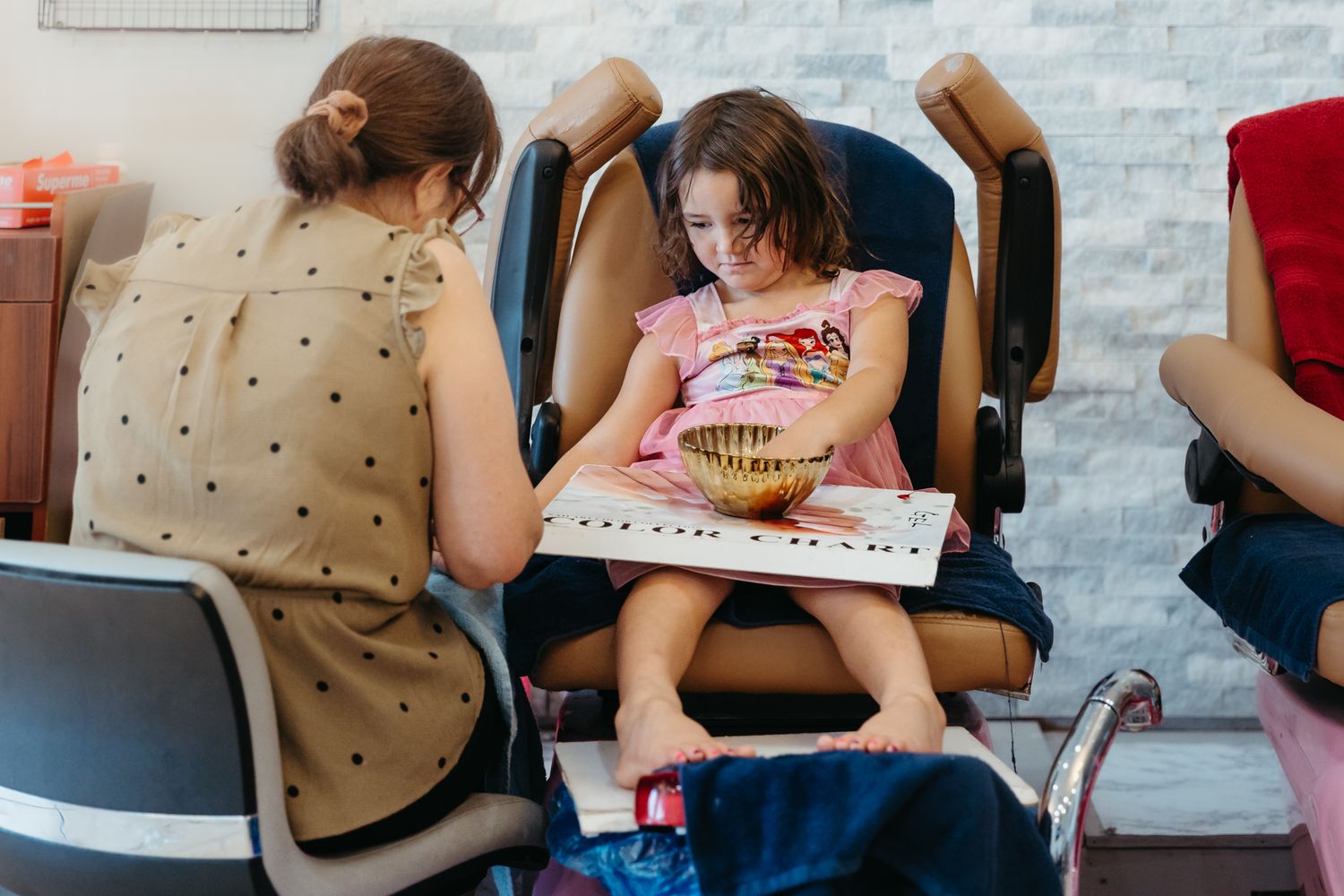 Close-up view of people sitting in dark gray and pink massage chairs while reading in a relaxation area.