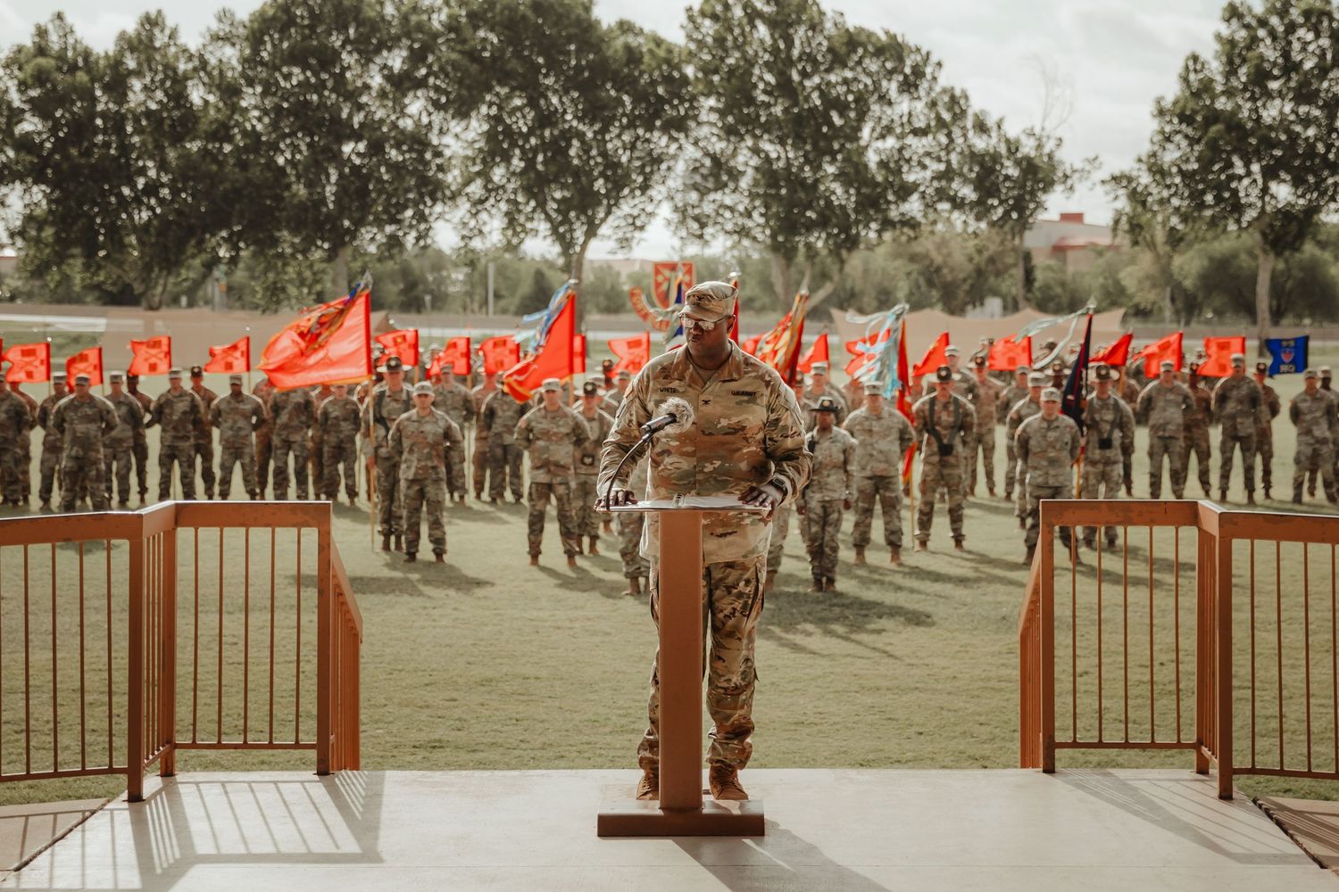 A panoramic view of military personnel gathered on a grassy field with trees in the background.