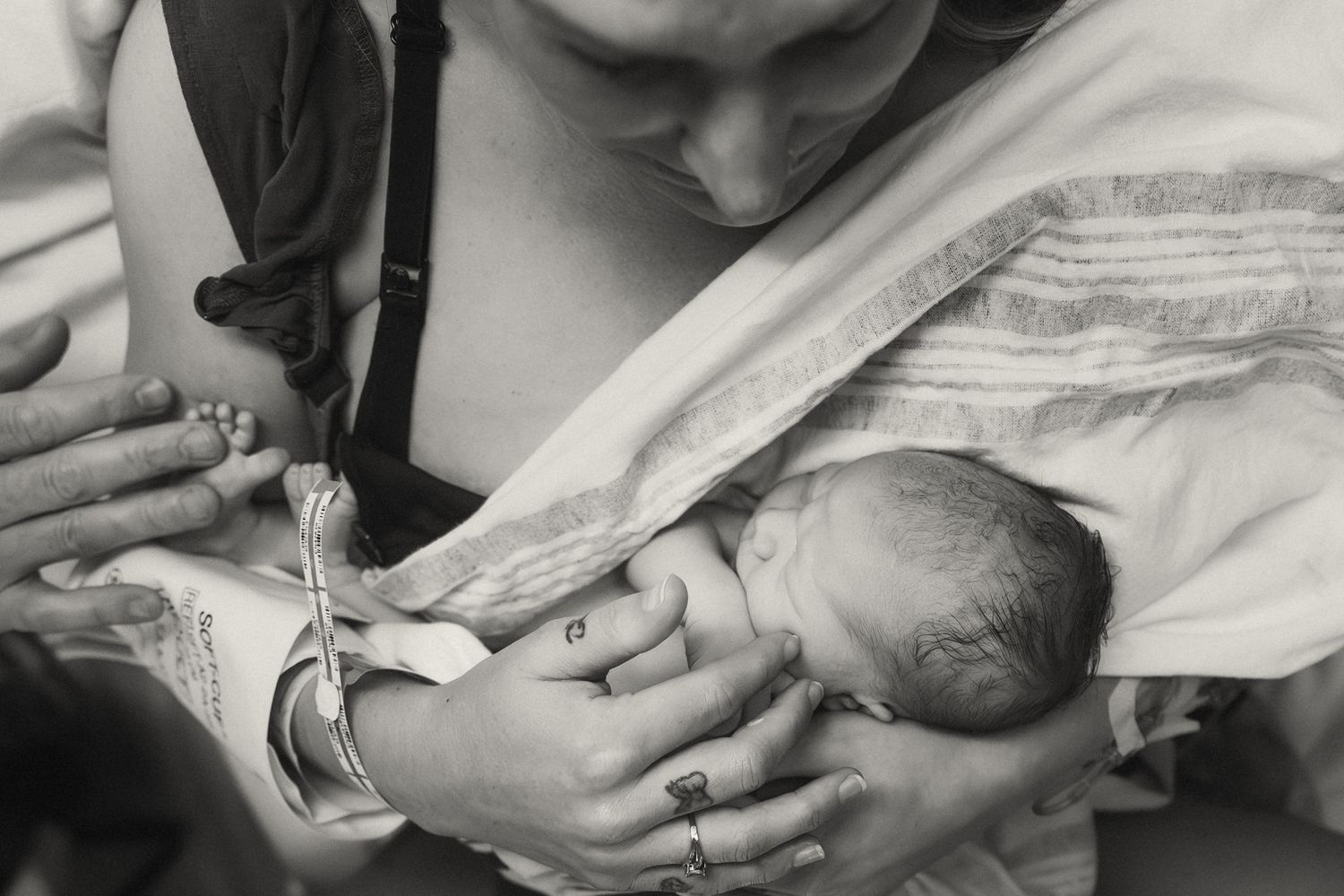 A black and white close-up photograph of mom and dad examining the details of their newborn in a hospital bed in Fort Still, Oklahoma by Liz