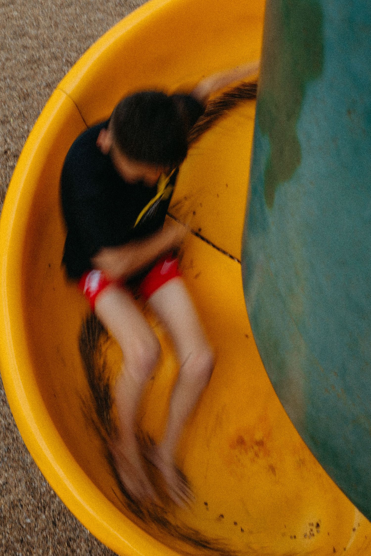 Child sliding down yellow playground slide captured with motion blur effect in action photography.