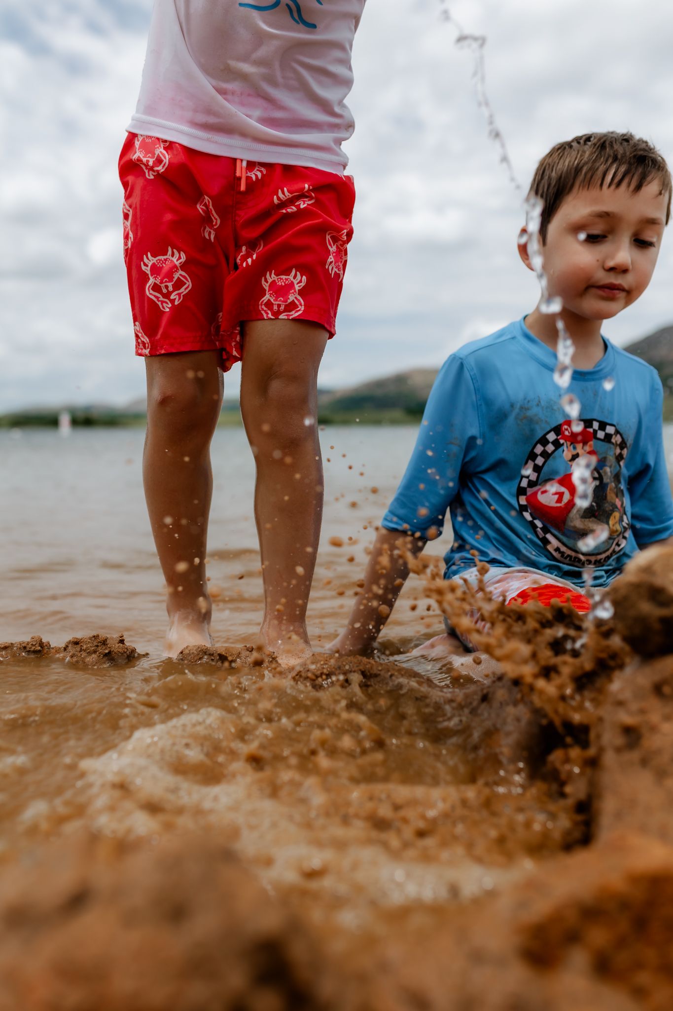 Kids splashing and playing in muddy water wearing colorful summer clothes.