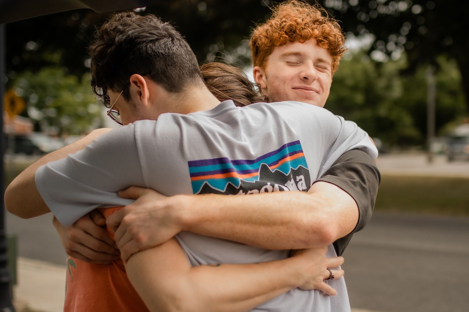 Friends sharing an emotional group hug outdoors wearing casual clothing.