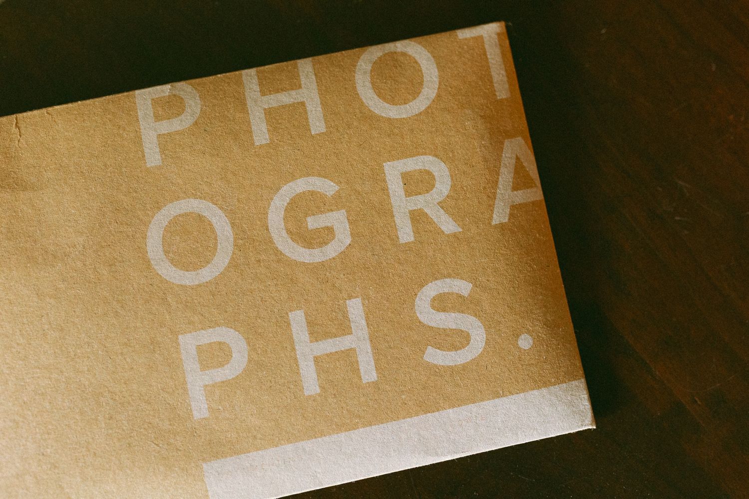 Brown kraft paper envelope with bold white text reading PHOTOGRAPHS on a dark wooden surface.