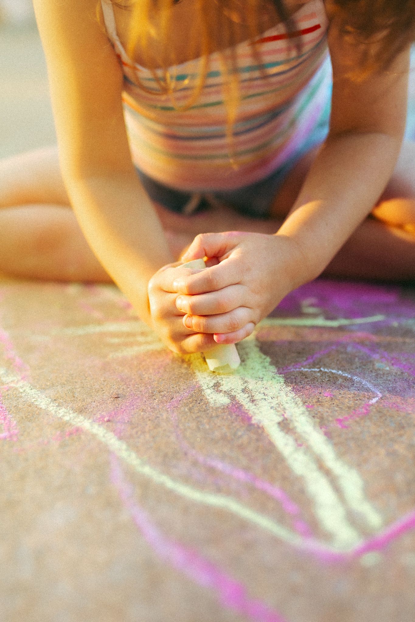 Hands drawing with colorful chalk on a sidewalk in sunlight.