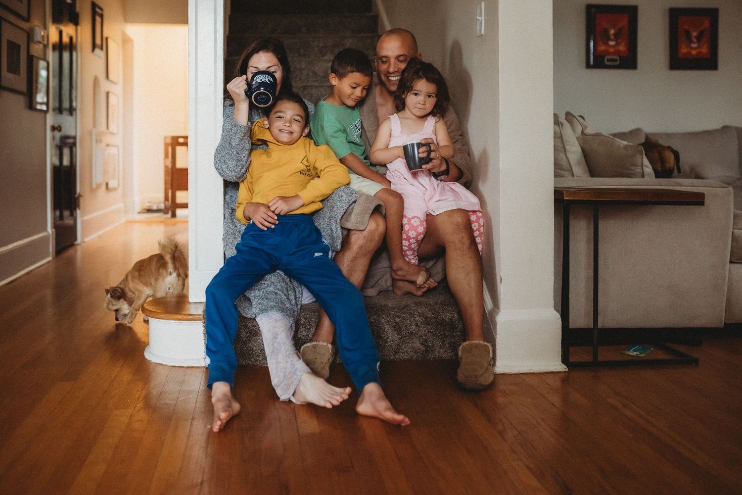 A group sits together on stairs inside a cozy home with hardwood floors while looking at a mobile device.