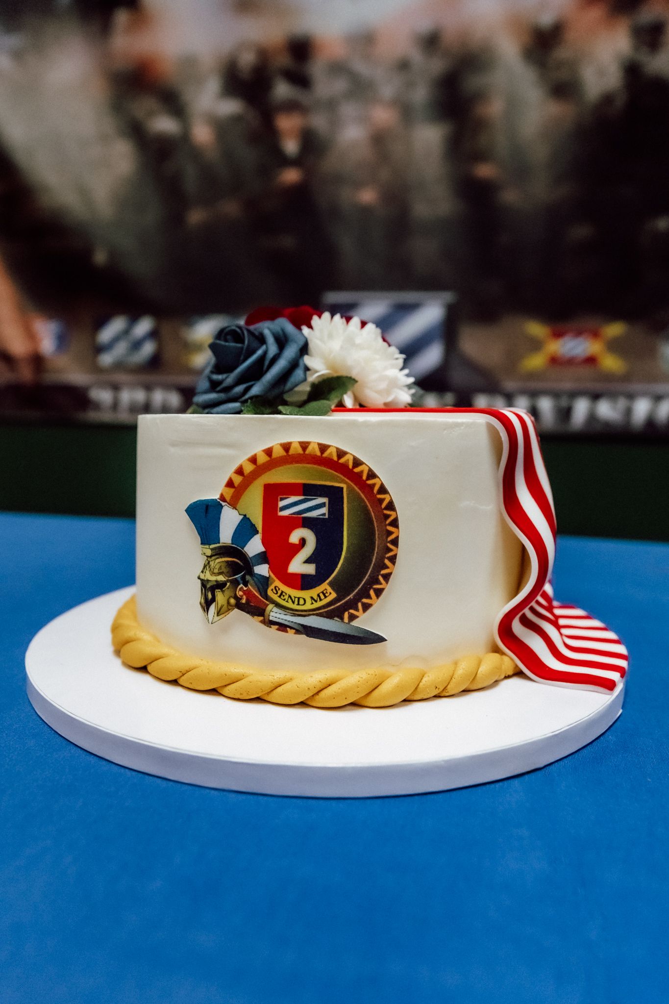 Decorative military-themed cake with emblems and American flag details displayed on a blue tablecloth.