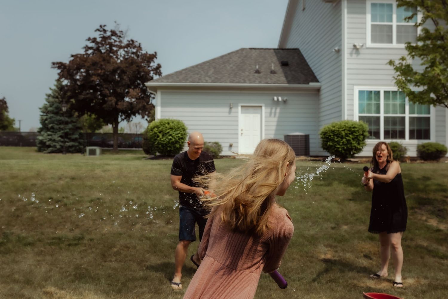 People engaging in a playful water gun battle in a suburban backyard setting.