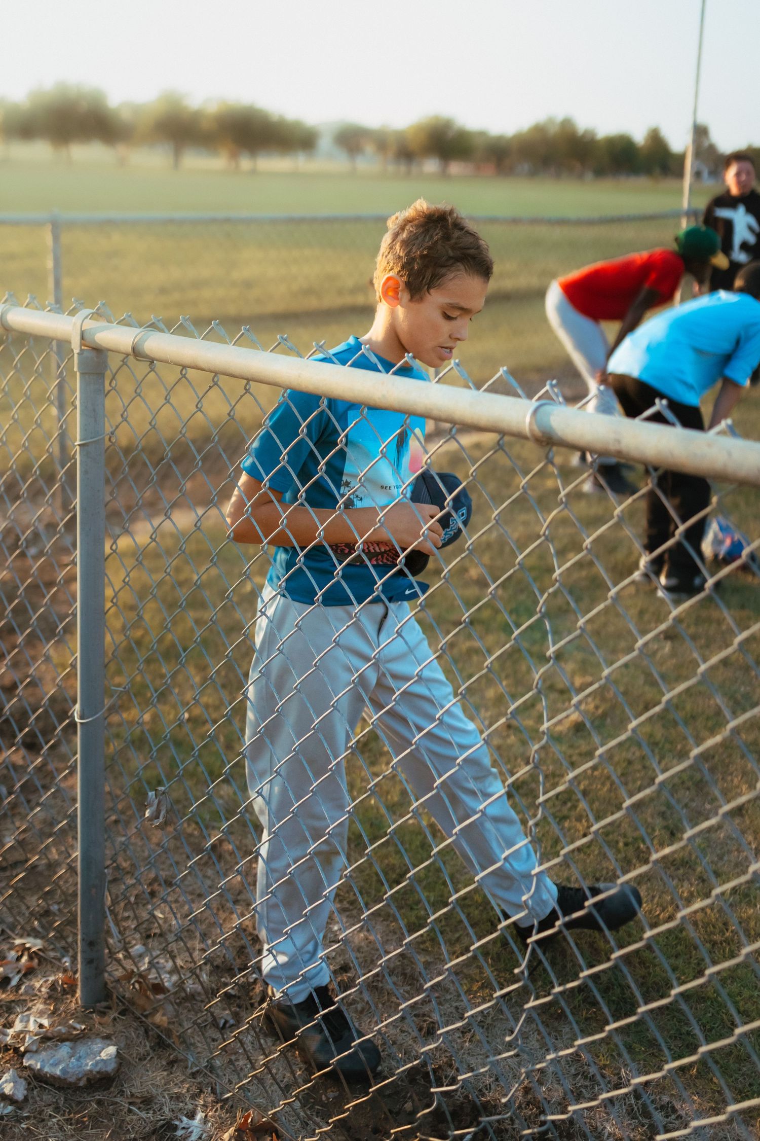 A person in a light blue shirt and jeans crouches down by a chain-link fence on a grassy field. Documentary Photographer Liz Perez