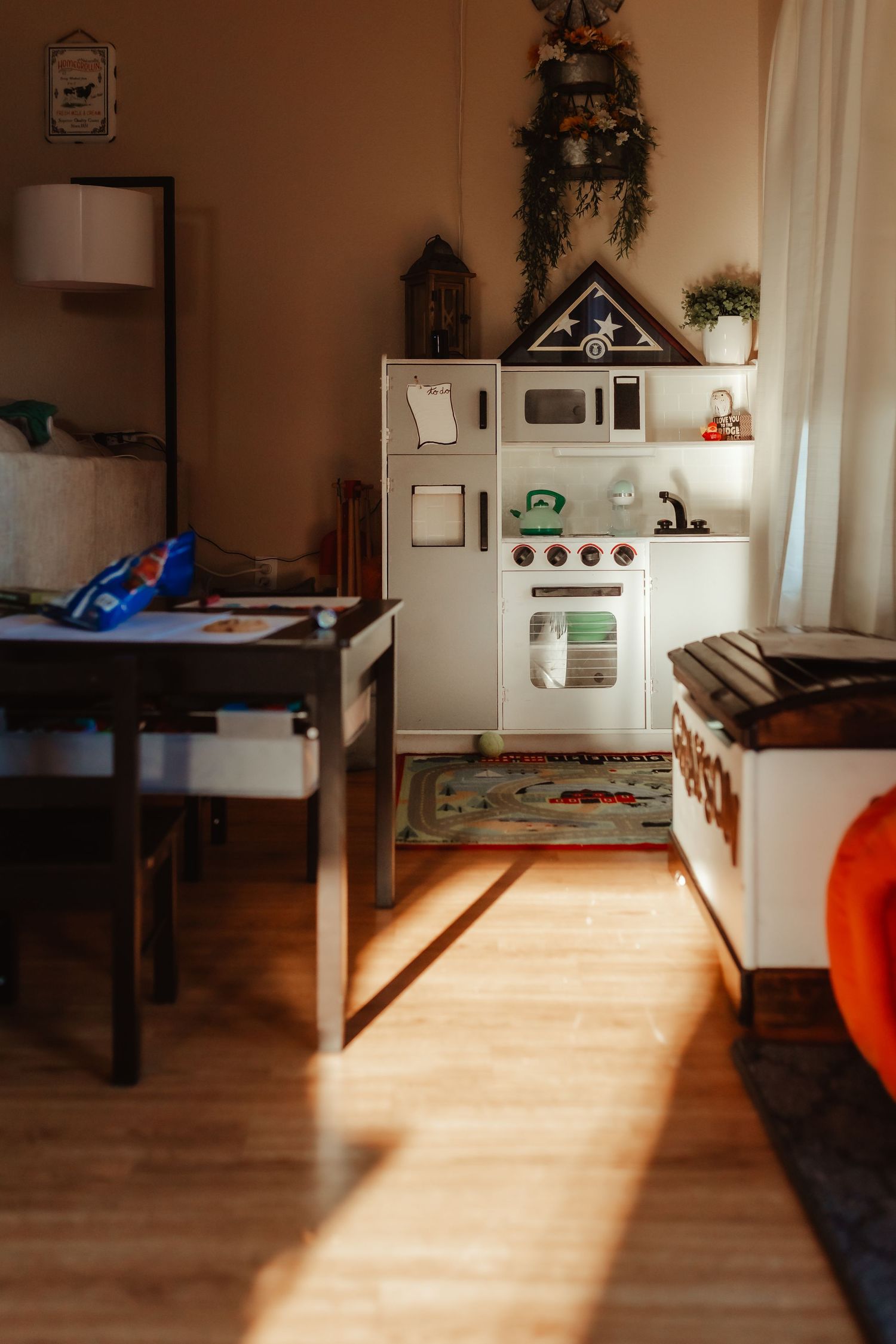 A children's play kitchen set in a sunlit corner with wooden flooring.