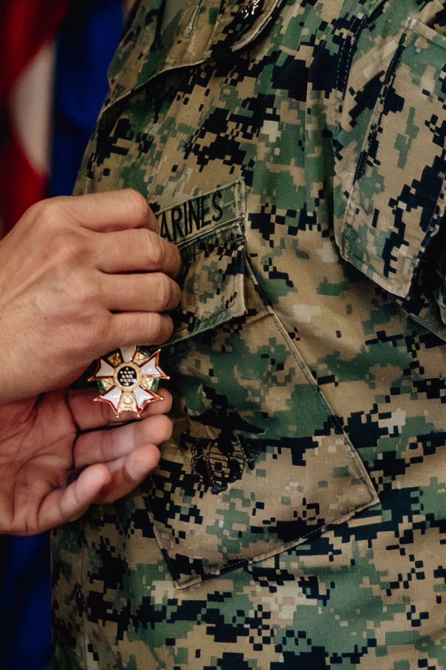 Marine in digital camo uniform holds a military medal during an award ceremony.