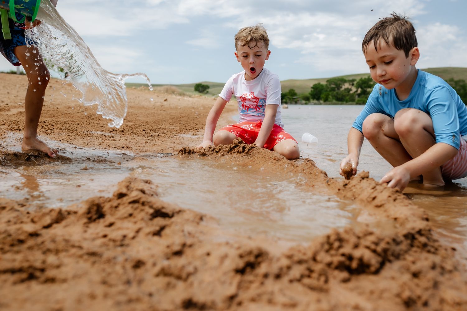 Children playing in wet sand at water's edge creating a sandcastle or beach activity.