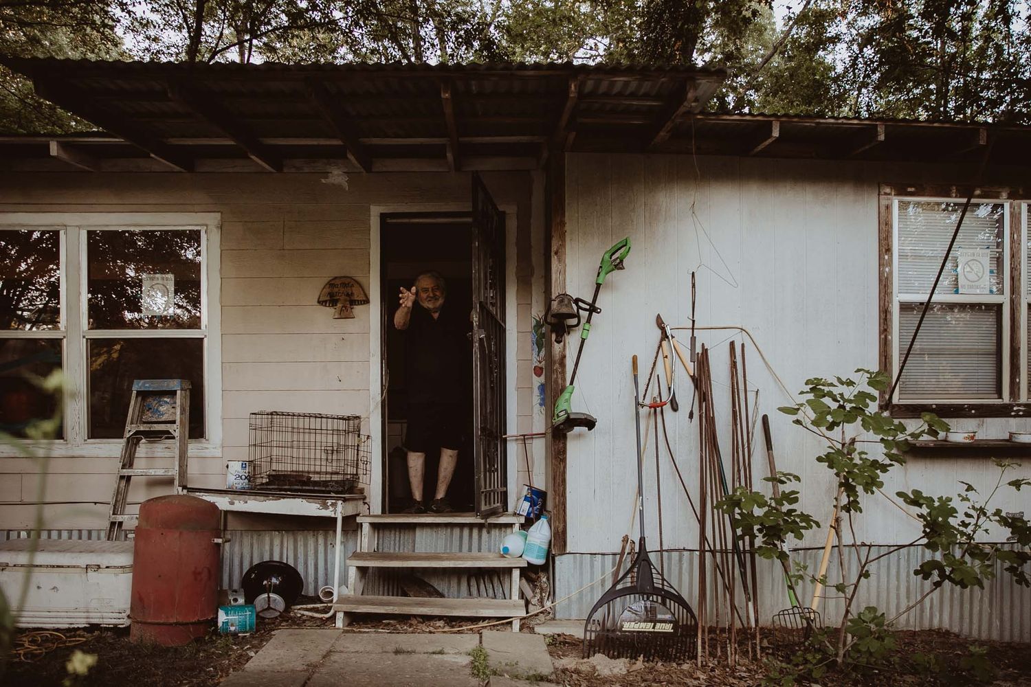 A moody shot of a small house exterior with a wooden porch and garden tools.