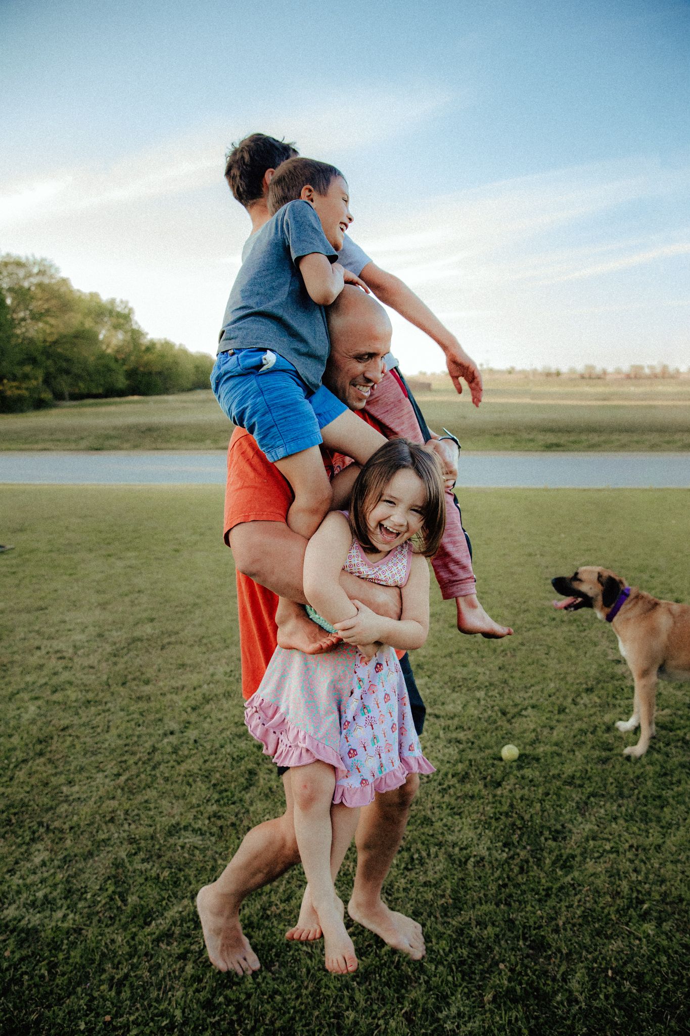 Family playing and laughing together in a grassy field at sunset.
