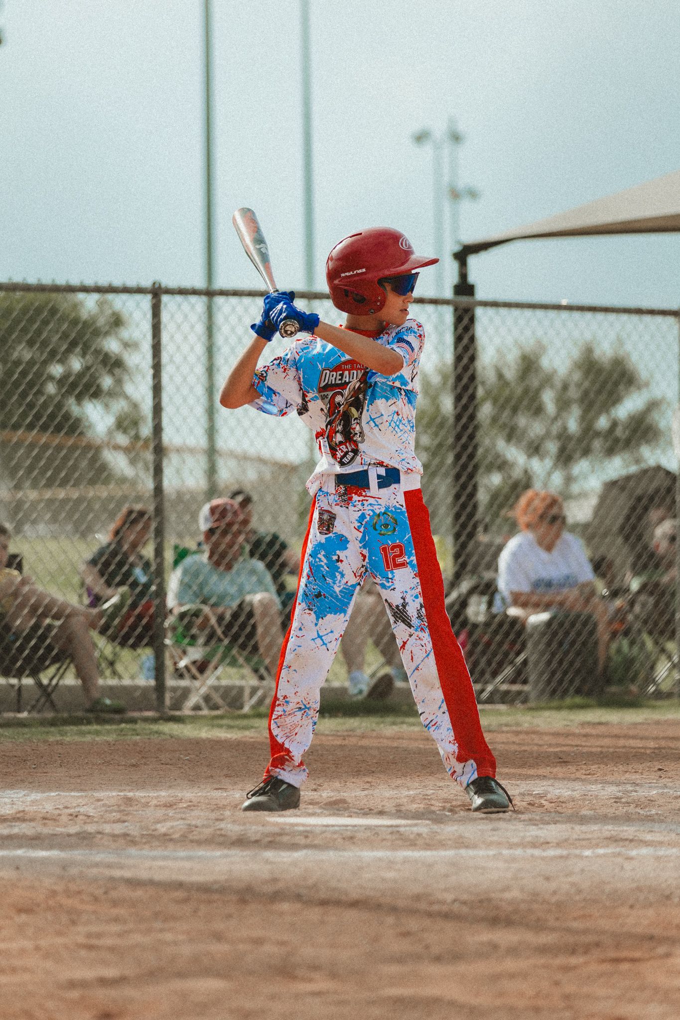 Young baseball player in colorful uniform and red helmet stands ready to bat at a Little League game.
