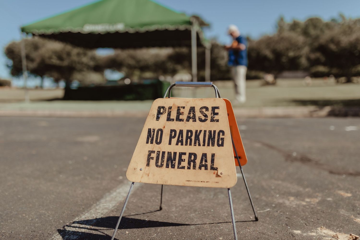 A wooden temporary sign reading 'Please No Parking Funeral' stands in an empty parking lot.
