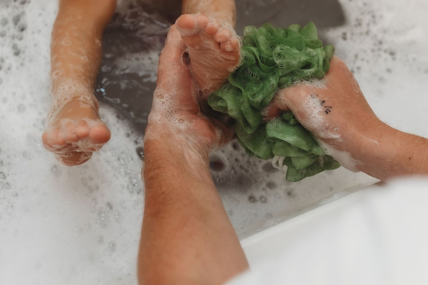 Hands washing fresh lettuce in soapy water at a sink.