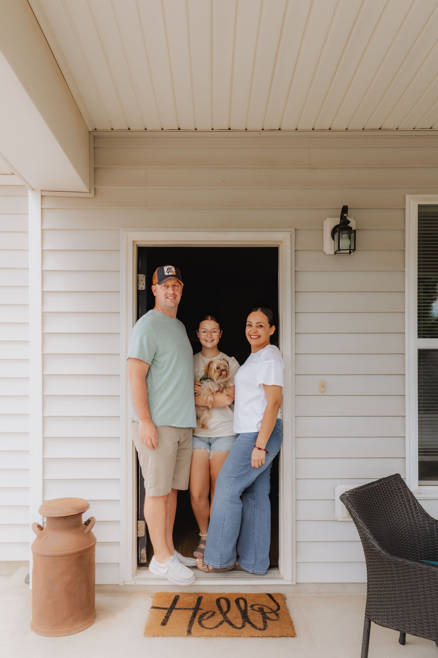 Family of three with a small dog posing at their front door with a Hello doormat on a home porch.