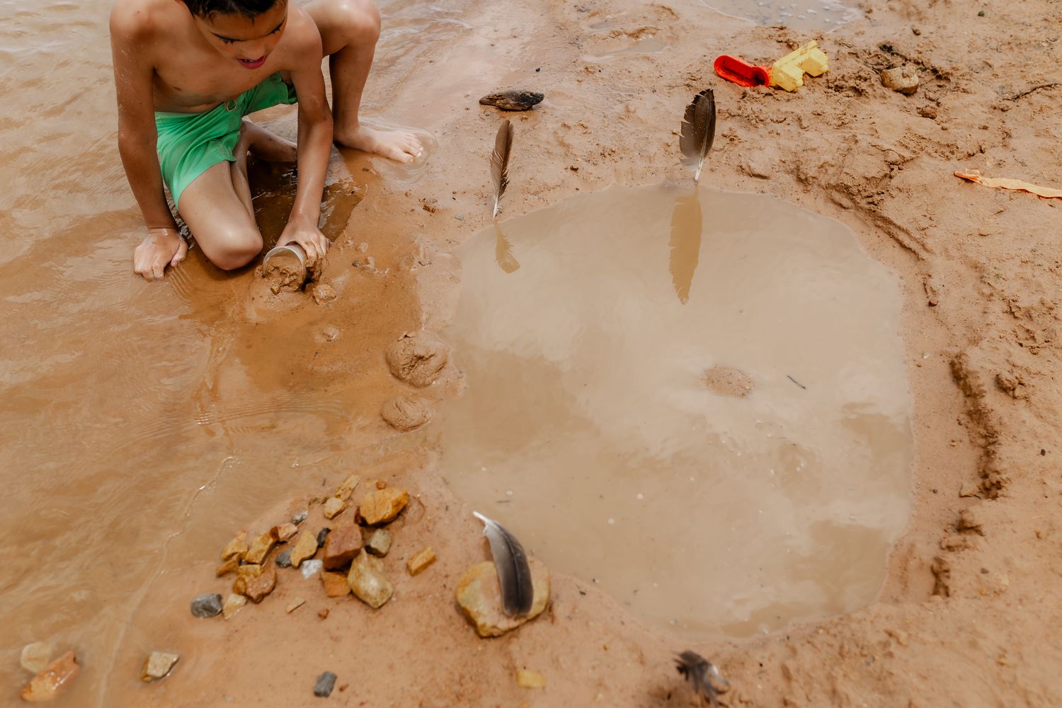 Person collecting shells and rocks around a puddle in wet sand.