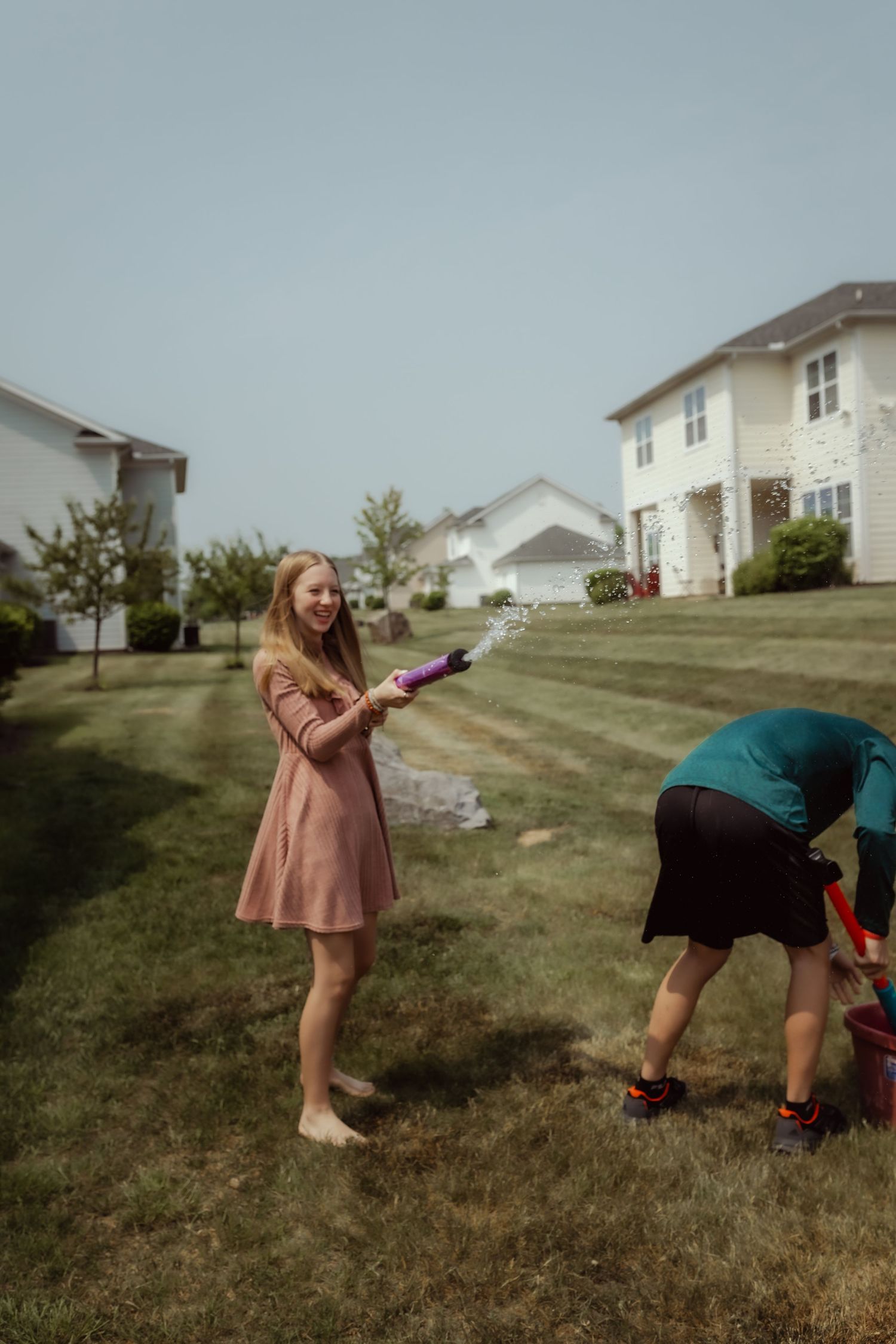 People enjoying a water gun fight in front of suburban homes on a summer day.