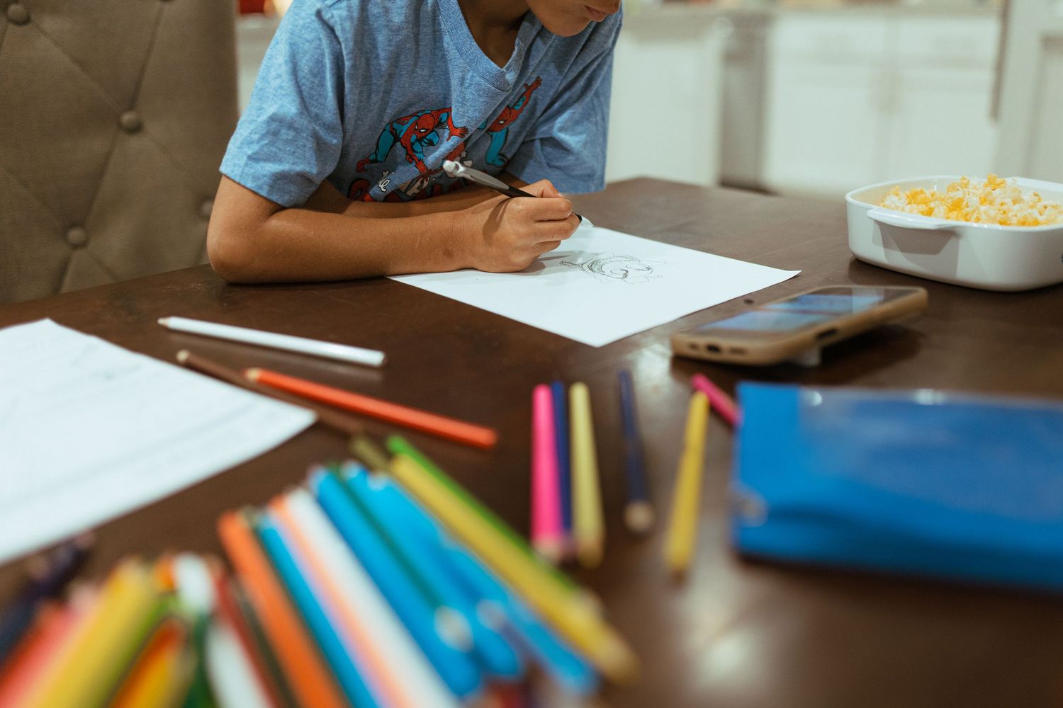 Students write and study with colorful school supplies and materials spread out on wooden desks in a classroom. In-Home Photography Liz Pere