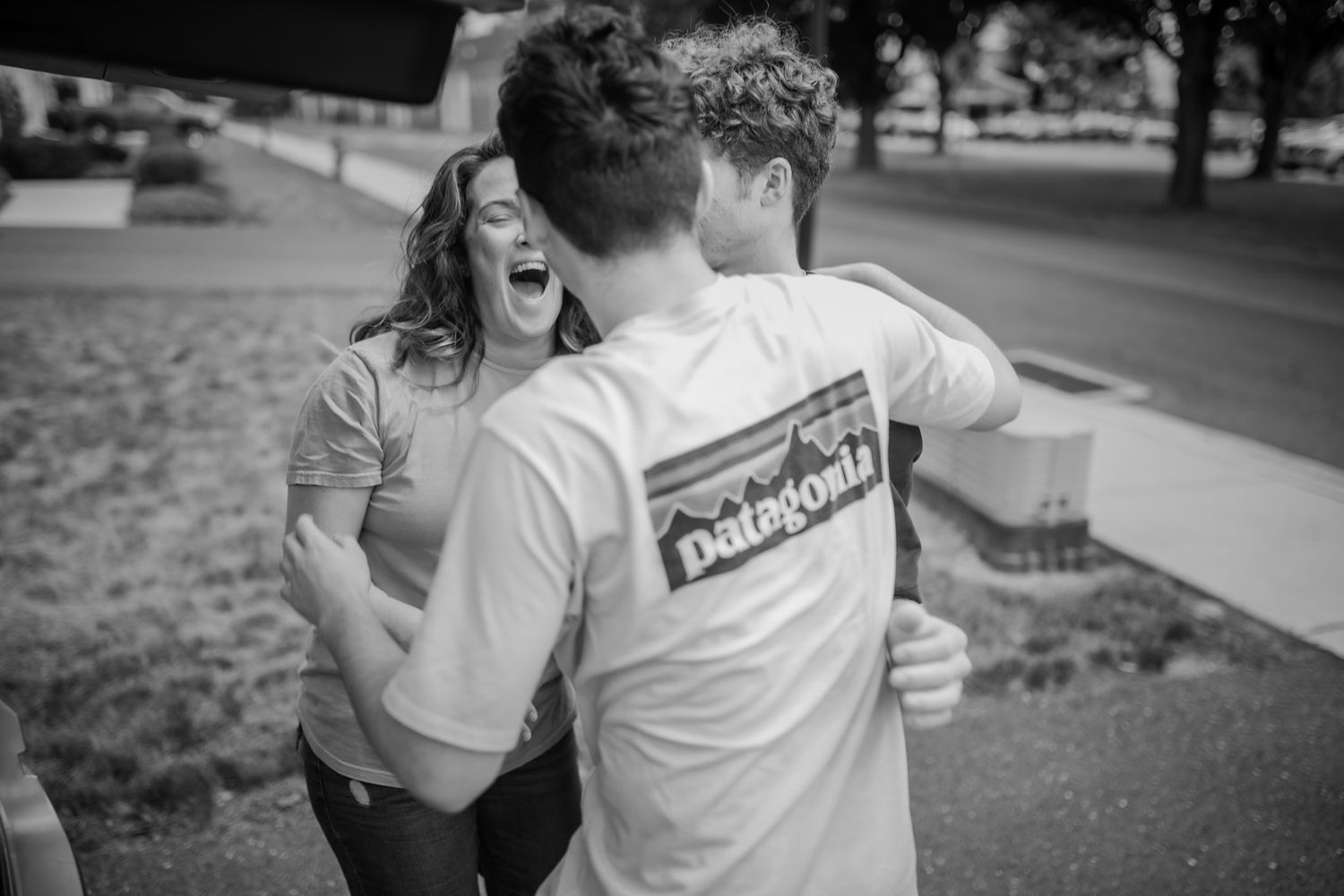 Black and white capture of friends sharing laughter and embraces outdoors.