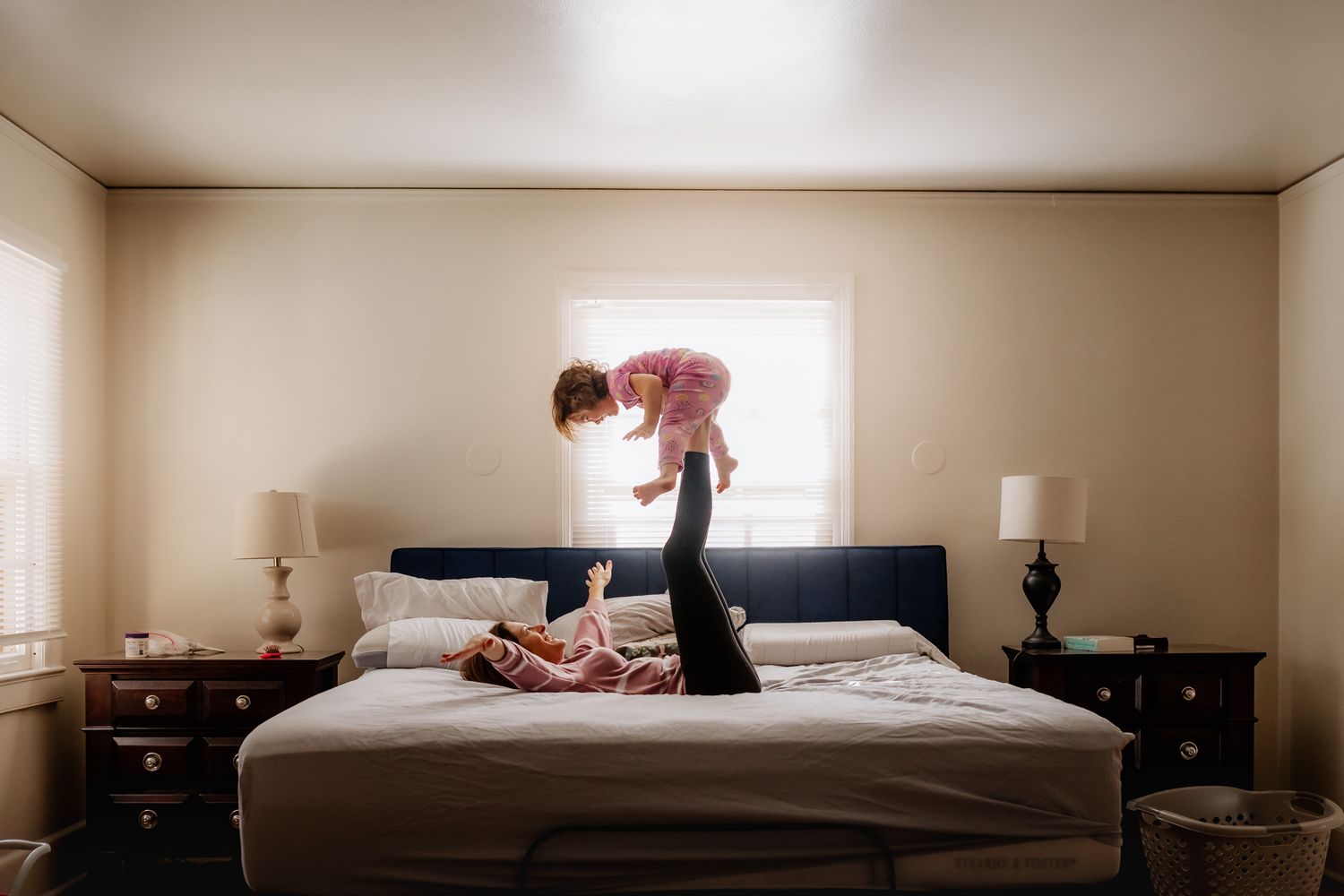 A playful scene on a bed in a sunlit bedroom with two figures engaged in a lighthearted moment.