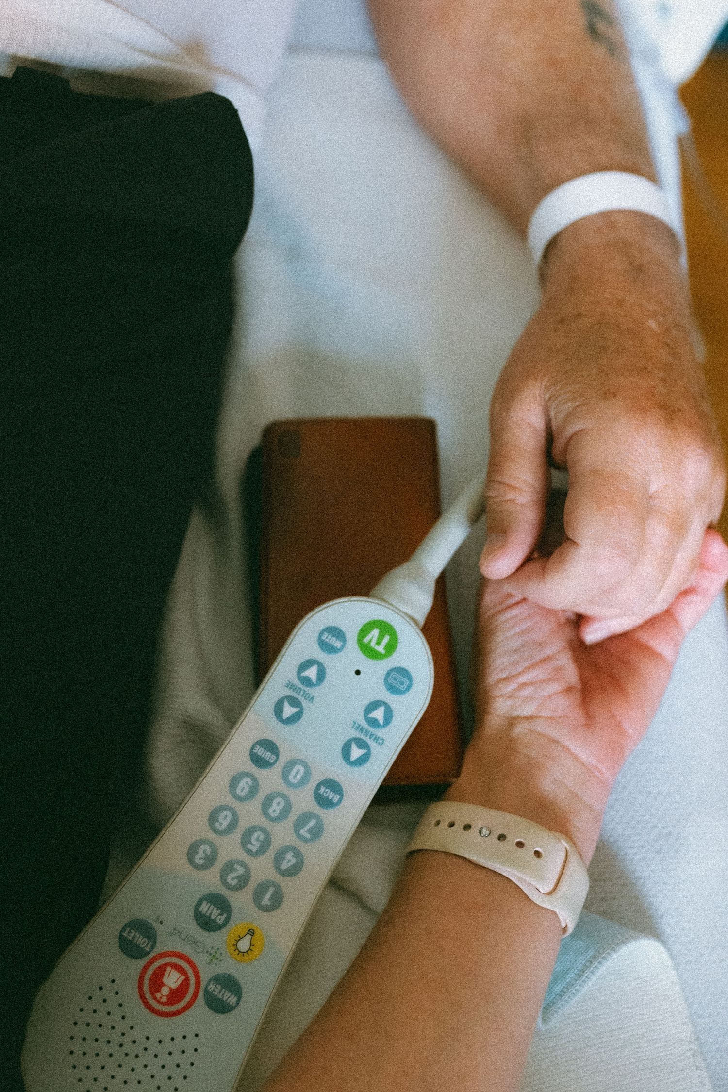 Person holding hands with hospital patient near medical remote control device.