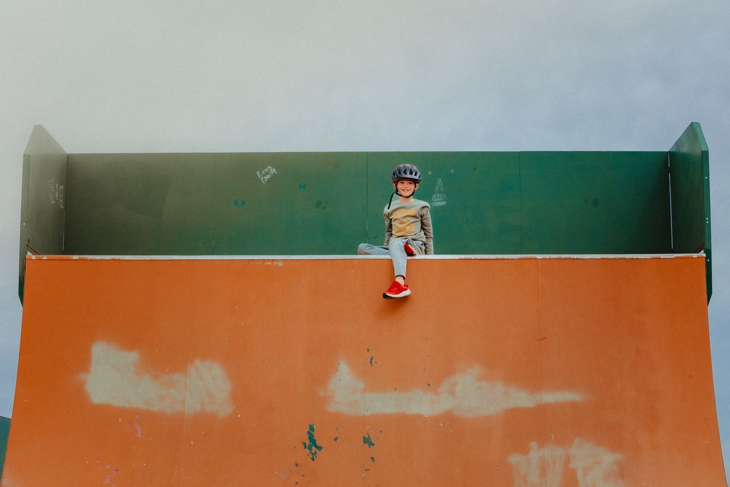 Small figure sitting atop an orange and green wall creating a striking geometric composition against solid background.