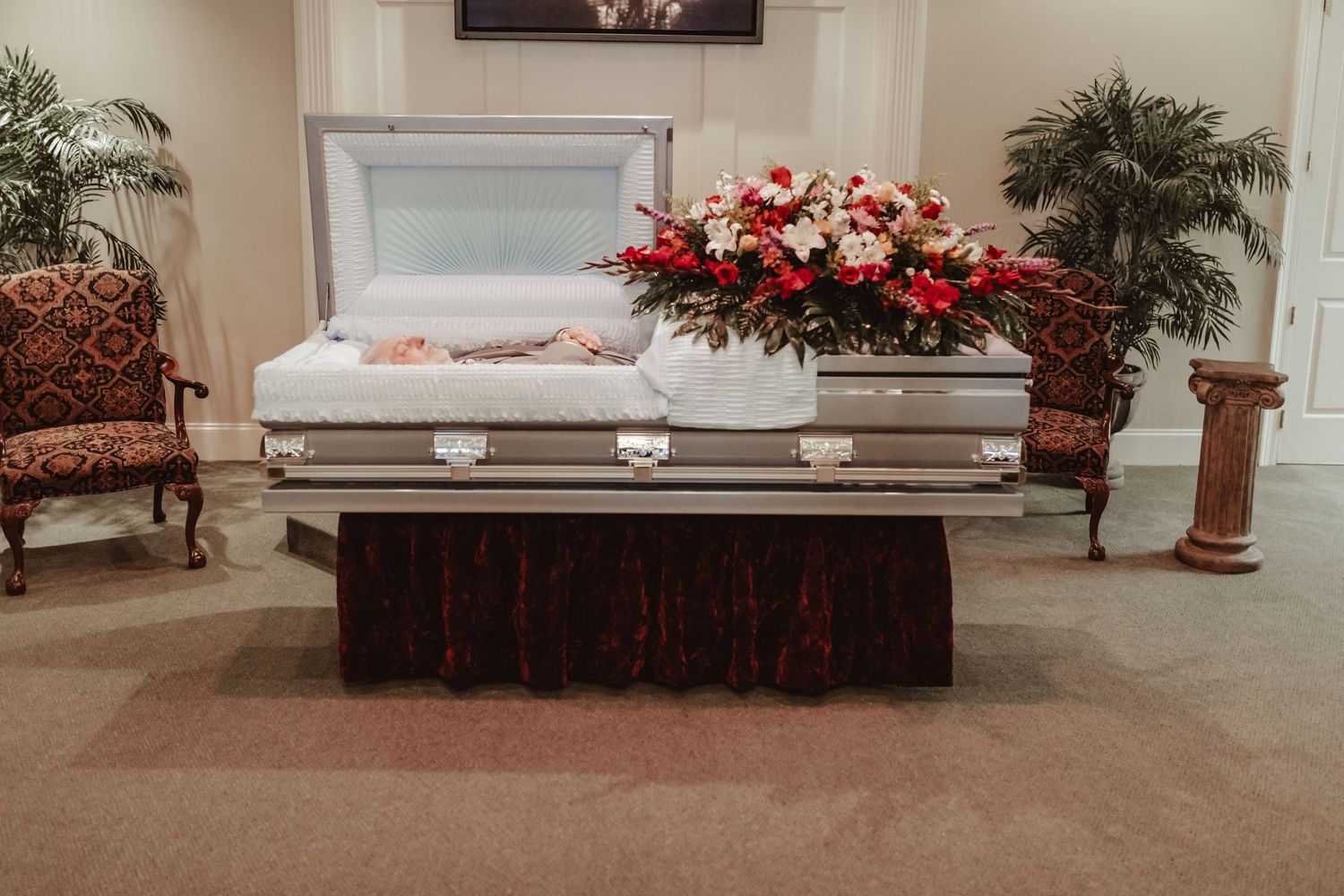 An elegant casket decorated with red and white floral arrangements displayed in a funeral home setting.
