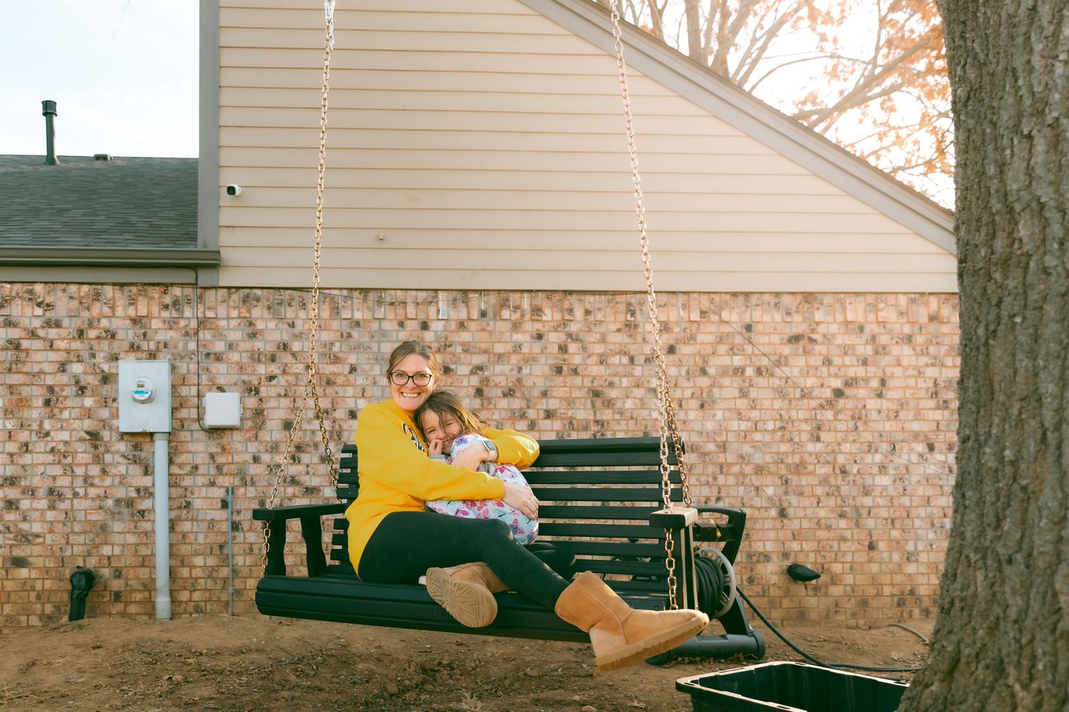 Person in yellow sweater sitting on green bench outside brick building.