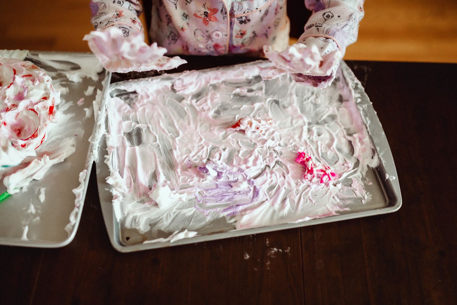 A metal tray covered in white frosting and pink decorative elements used for cake decorating.
