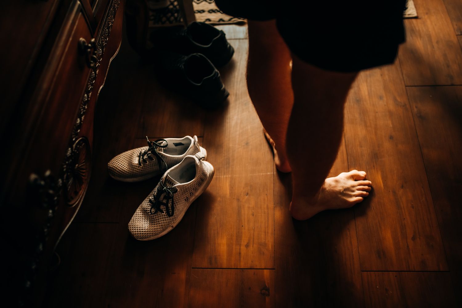 Shoes on hardwood floor next to bare feet in low-light setting. In-Home Photography Liz Perez