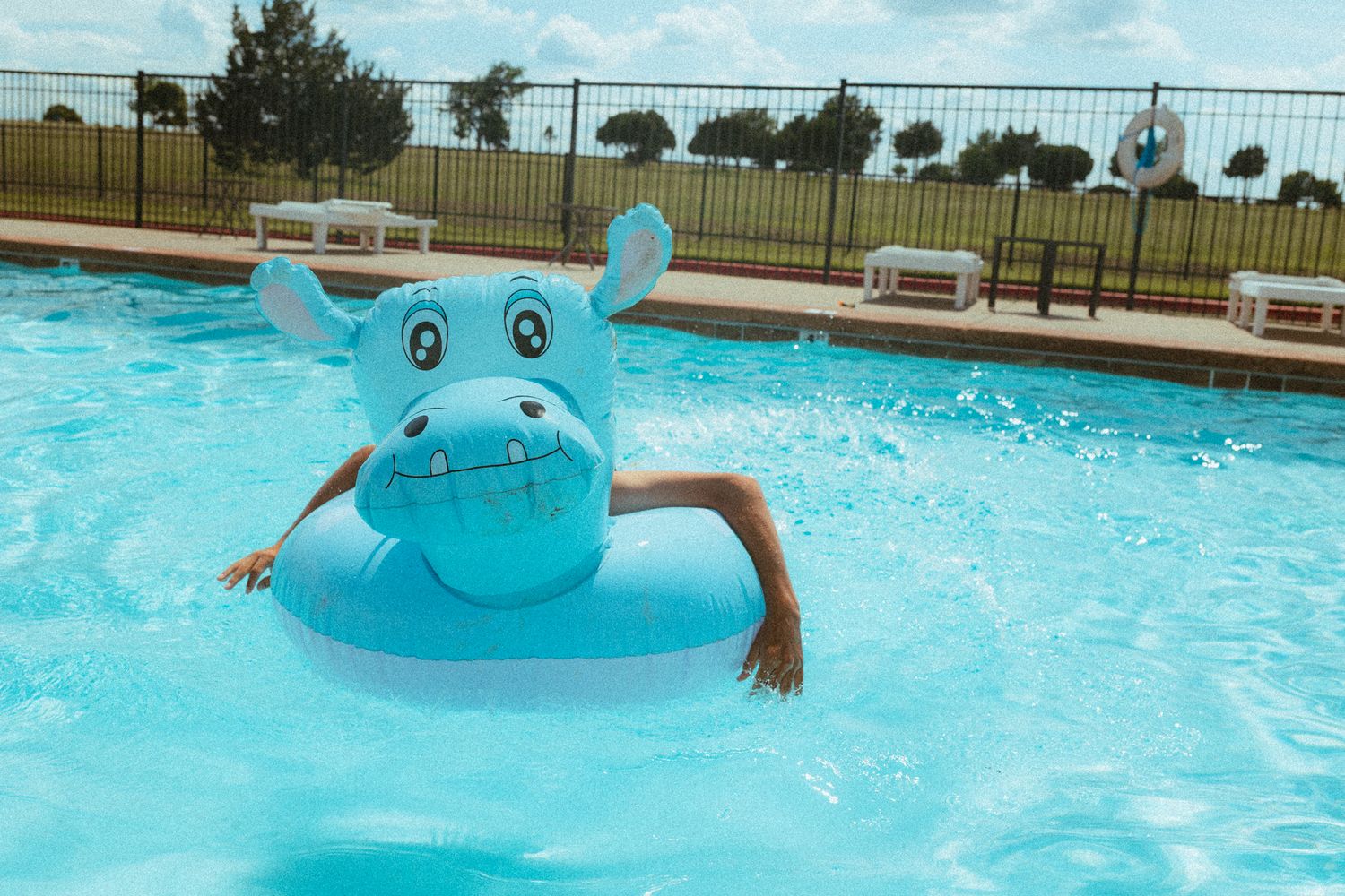 Child playing in a swimming pool with a blue hippo inflatable float ring on a sunny day.