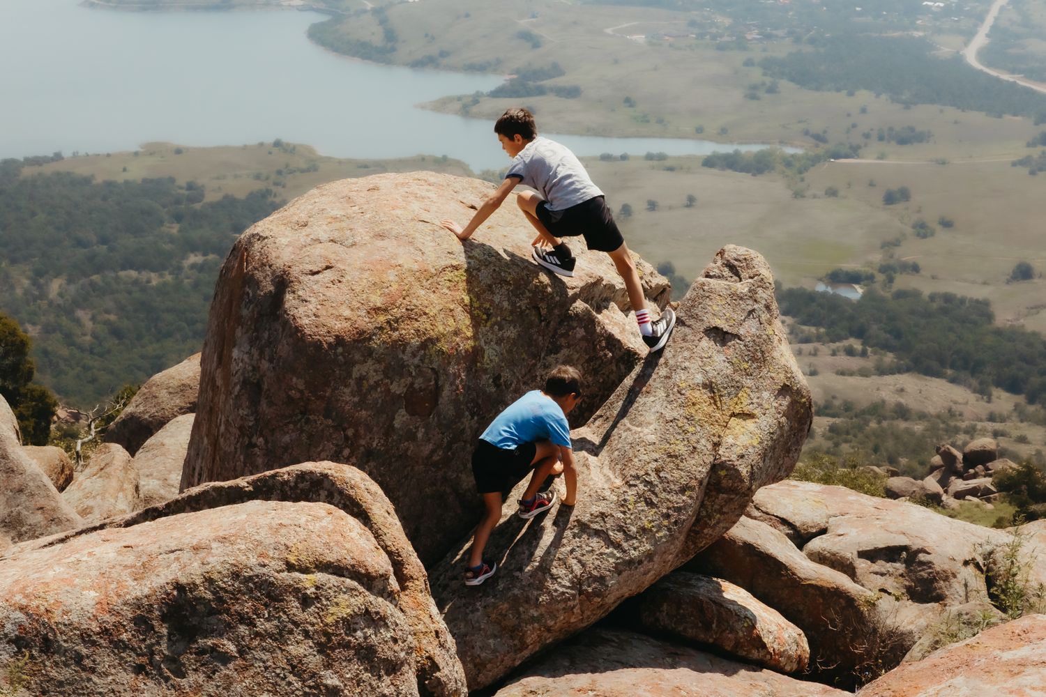 Rock climbers traverse scenic mountain terrain across multiple boulders in natural outdoor setting.