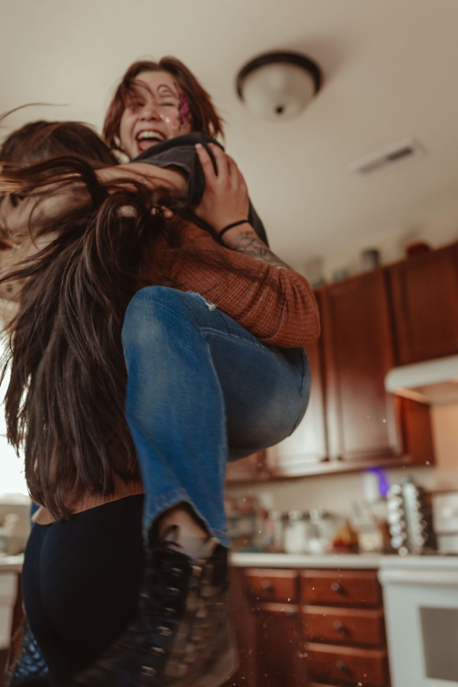 Two people hugging and laughing in a kitchen with dramatic lighting.