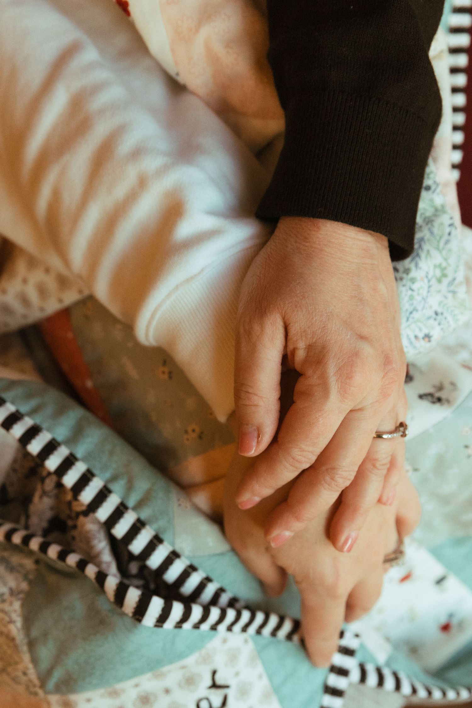 Close up of hands holding each other on a patterned blanket with stripes.