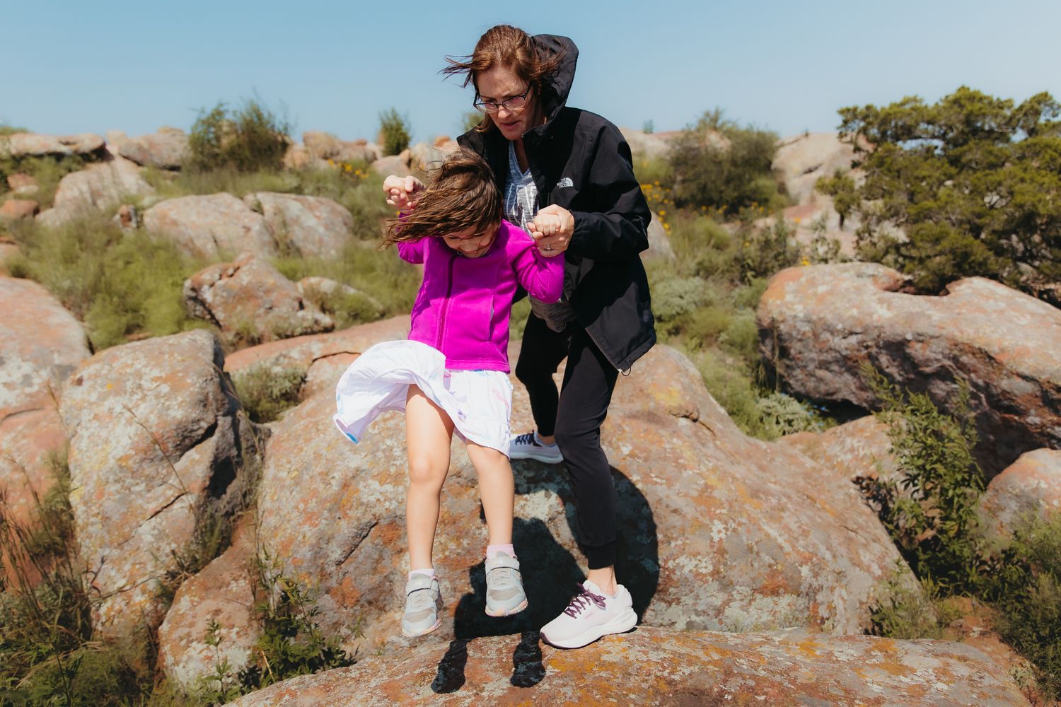 People climbing over large boulders in a scenic outdoor setting during a hiking adventure. In-Home Photography Liz Perez