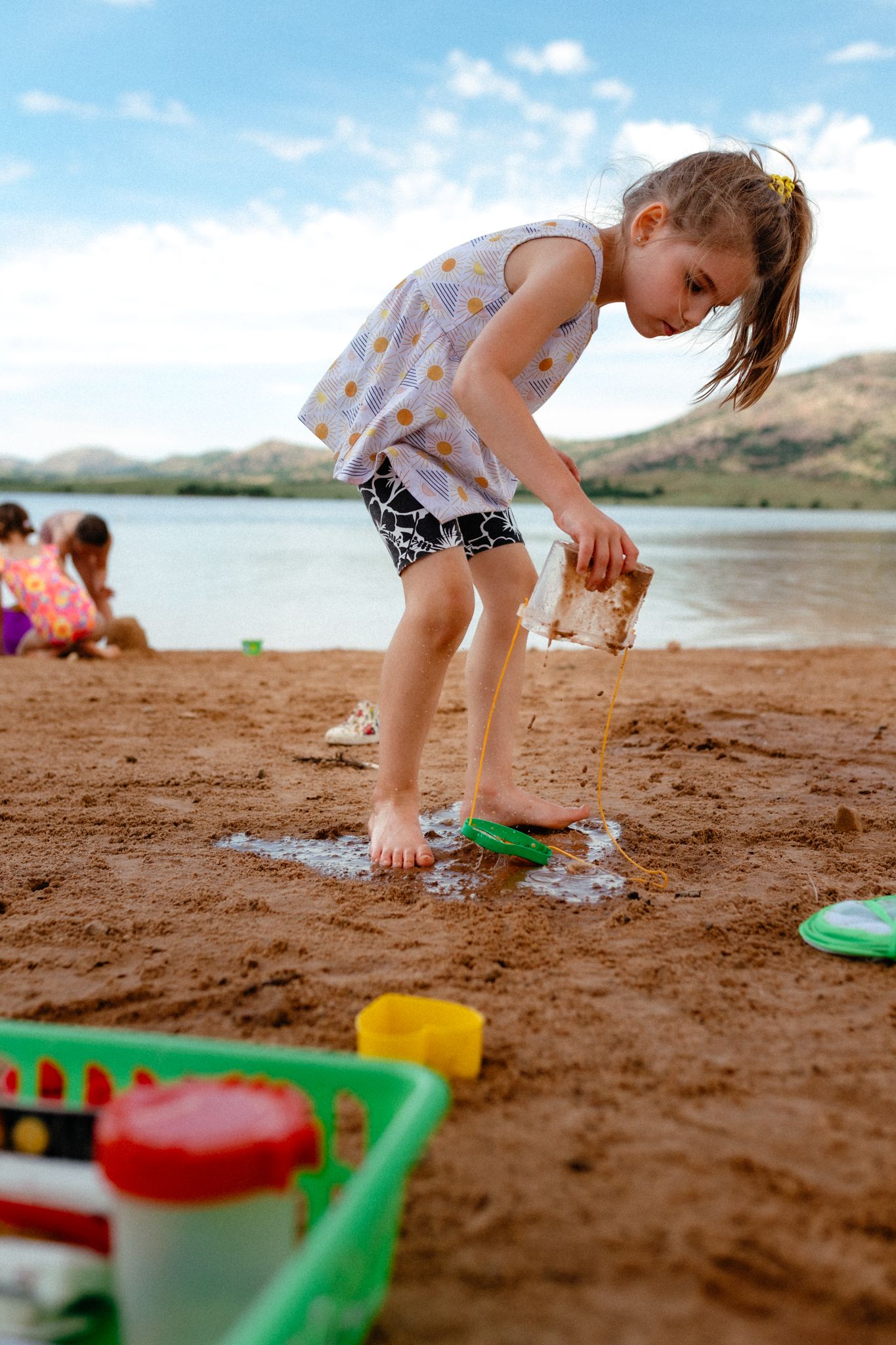 Child playing with sand toys at a lakeside beach on a sunny summer day.