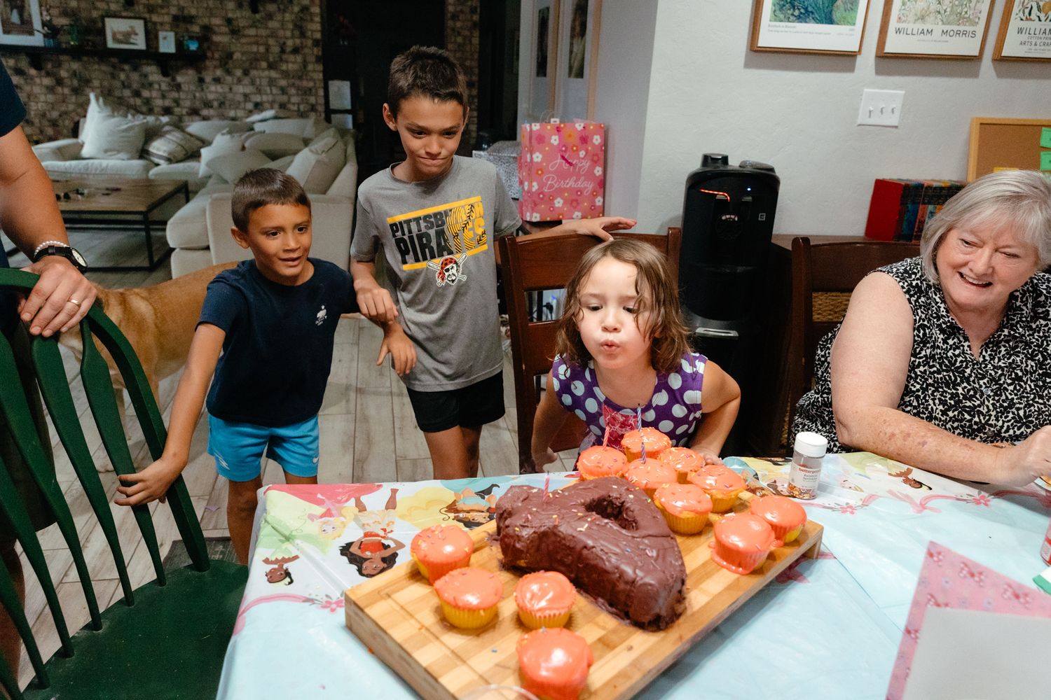 A birthday party scene showing guests gathered around a table with chocolate cake and decorations.