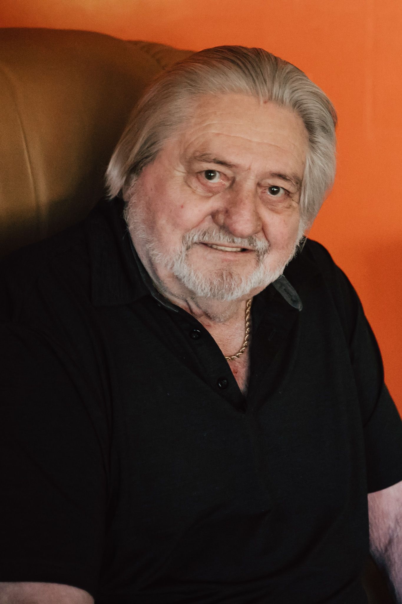 Portrait of senior man with white hair and beard against orange wall.