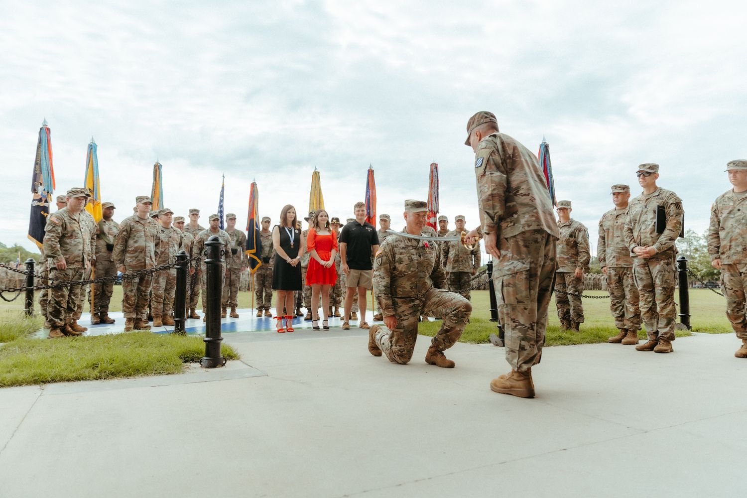 Military personnel stand in formation during an outdoor ceremony on a grassy field.