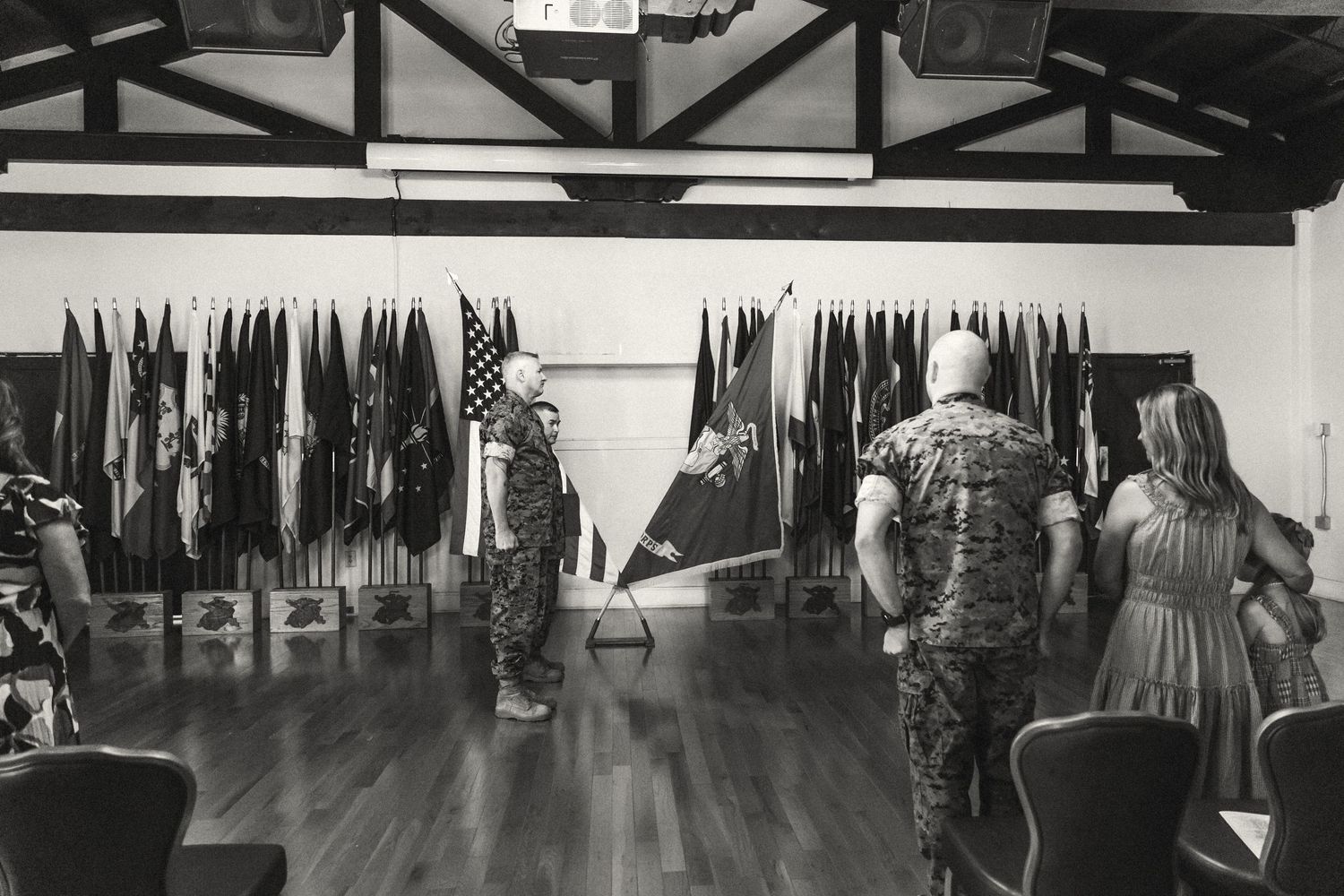 Black and white photo of military personnel and family viewing rows of flags in a ceremonial hall.