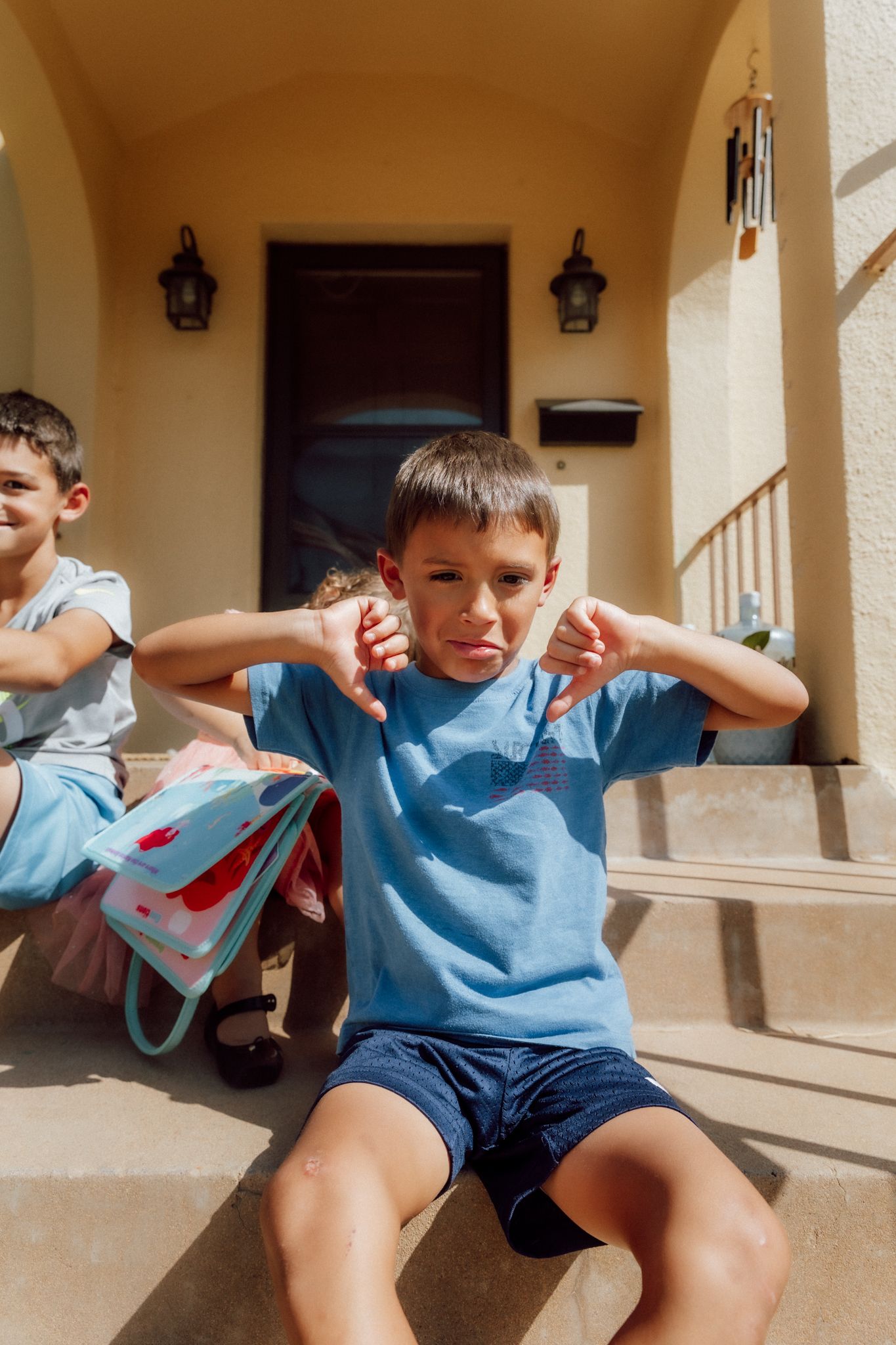 Children hanging out on front porch steps wearing light blue and navy outfits on a sunny afternoon.