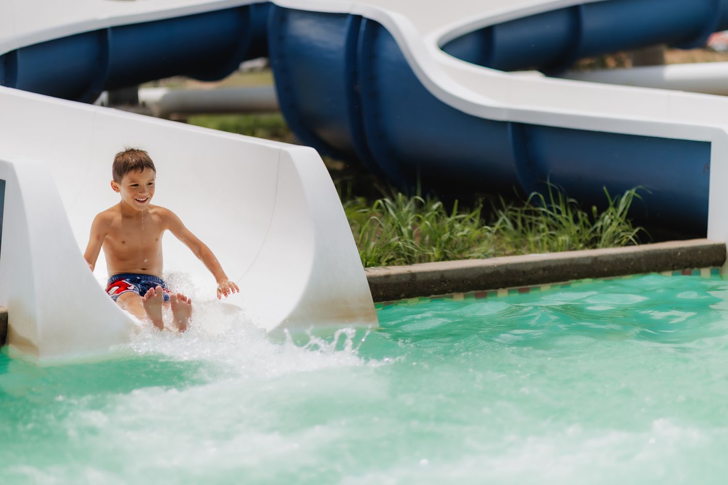 Child sliding down blue and white water slide into pool with splash.