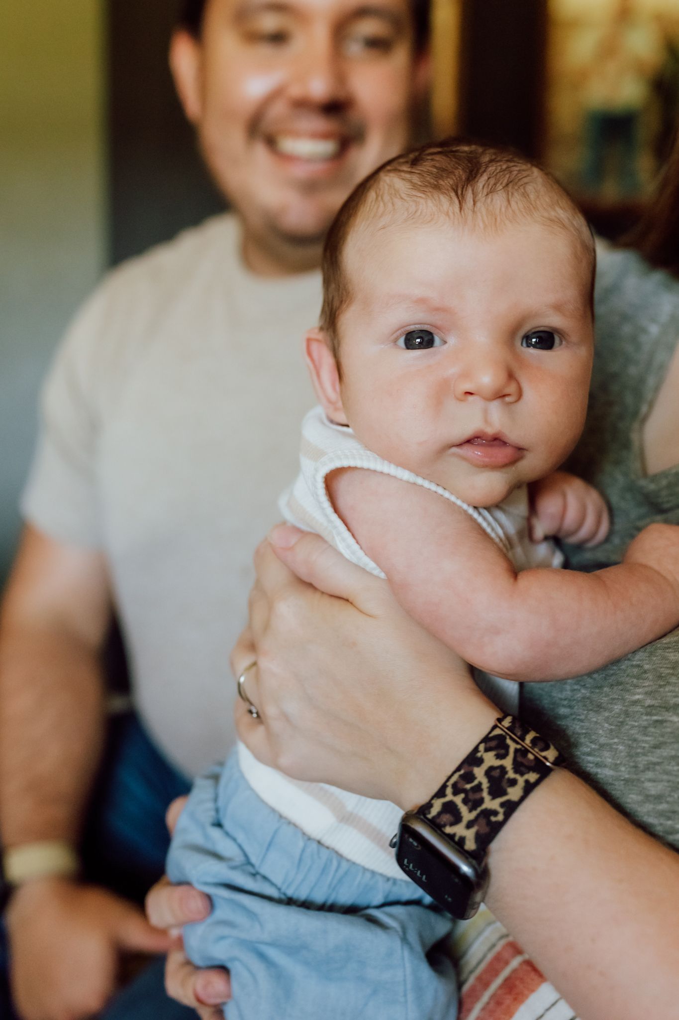 Baby wearing blue shorts and white top looks at camera while being held.