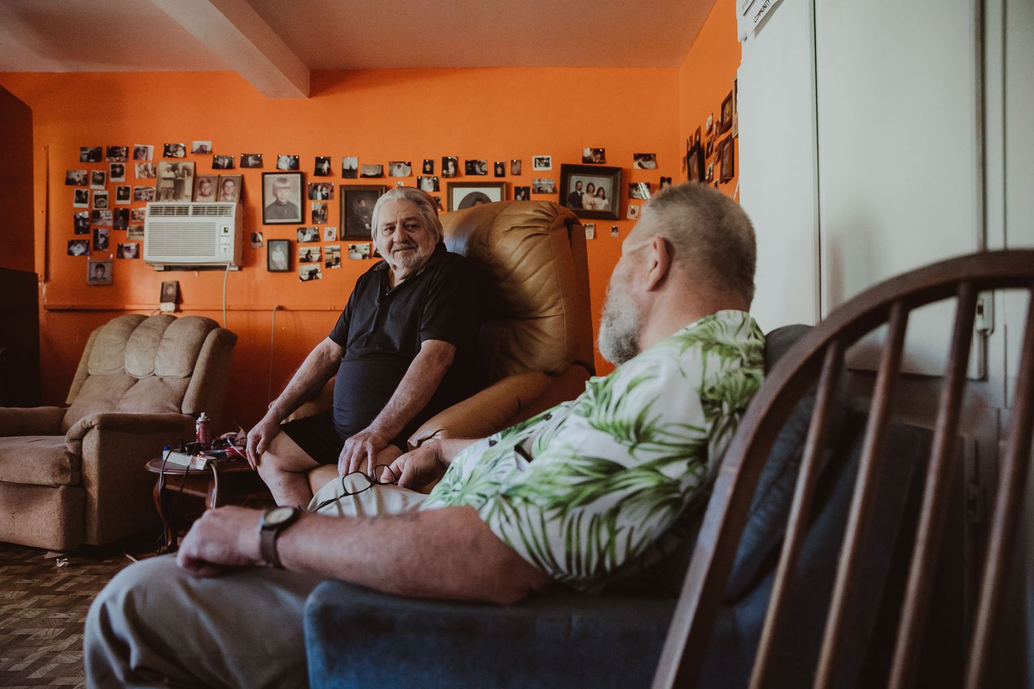 People relaxing in armchairs in a room with bright orange walls covered in photographs.