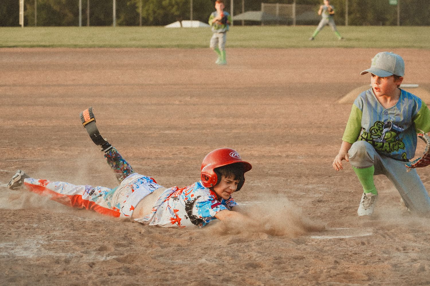 Young baseball player slides into base as fielder reaches to make the tag during a youth baseball game.