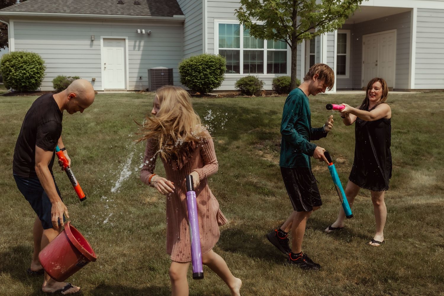 Family of four having a fun water gun fight in their backyard on a sunny summer day.