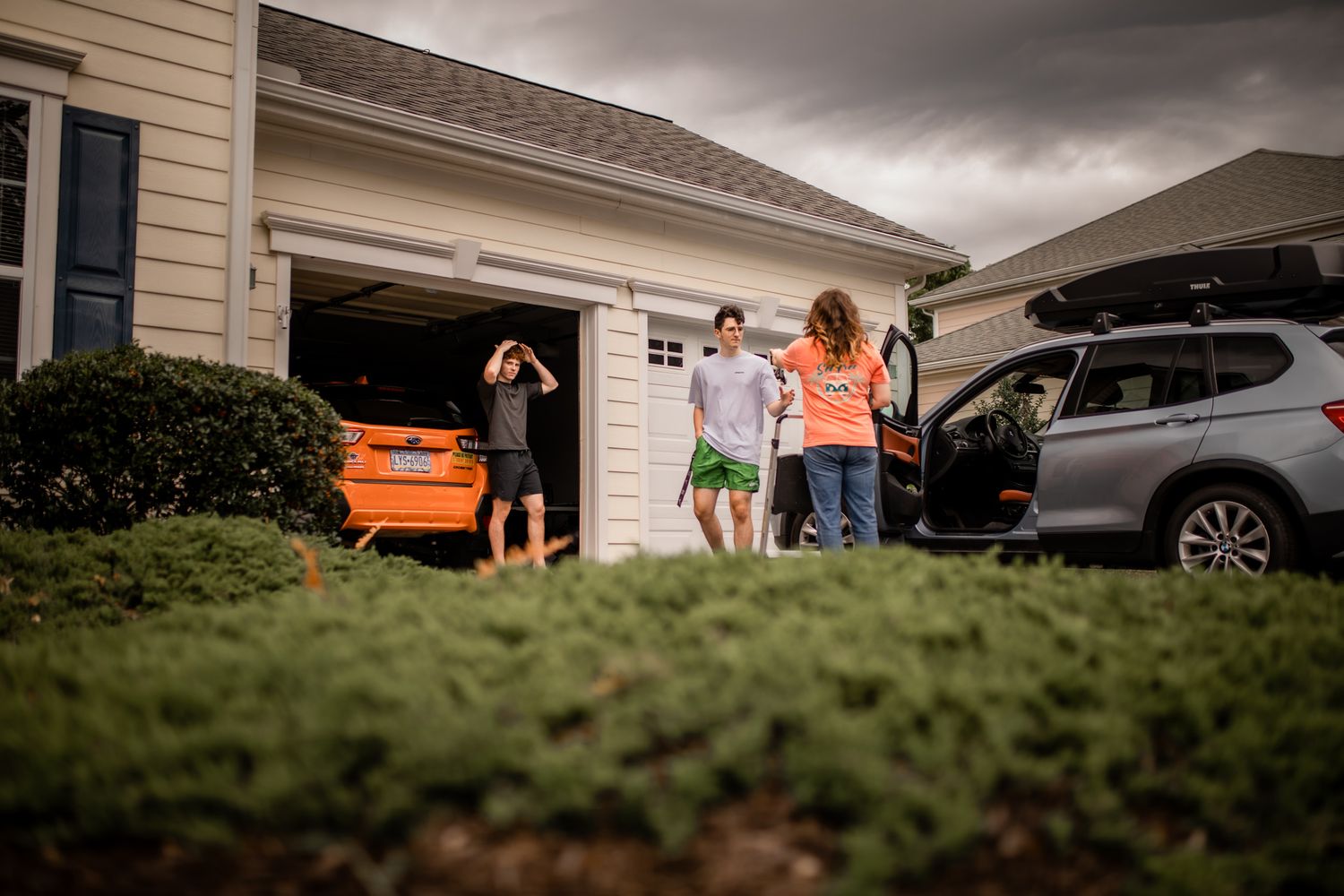 Group of friends gathered outside a residential home with cars parked in the driveway.